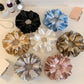 Close-up of Gifty elegant satin ruffle scrunchie in soft pink on white background