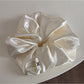 Glossy satin scrunchie in pink on a neutral background with soft shadows