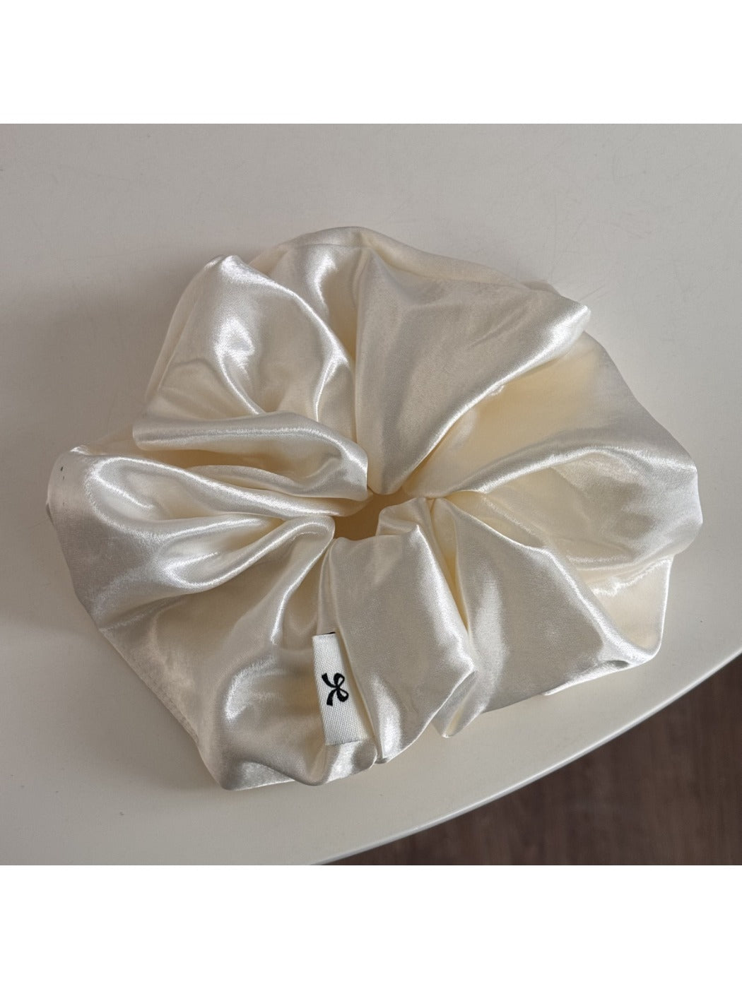 Glossy satin scrunchie in pink on a neutral background with soft shadows