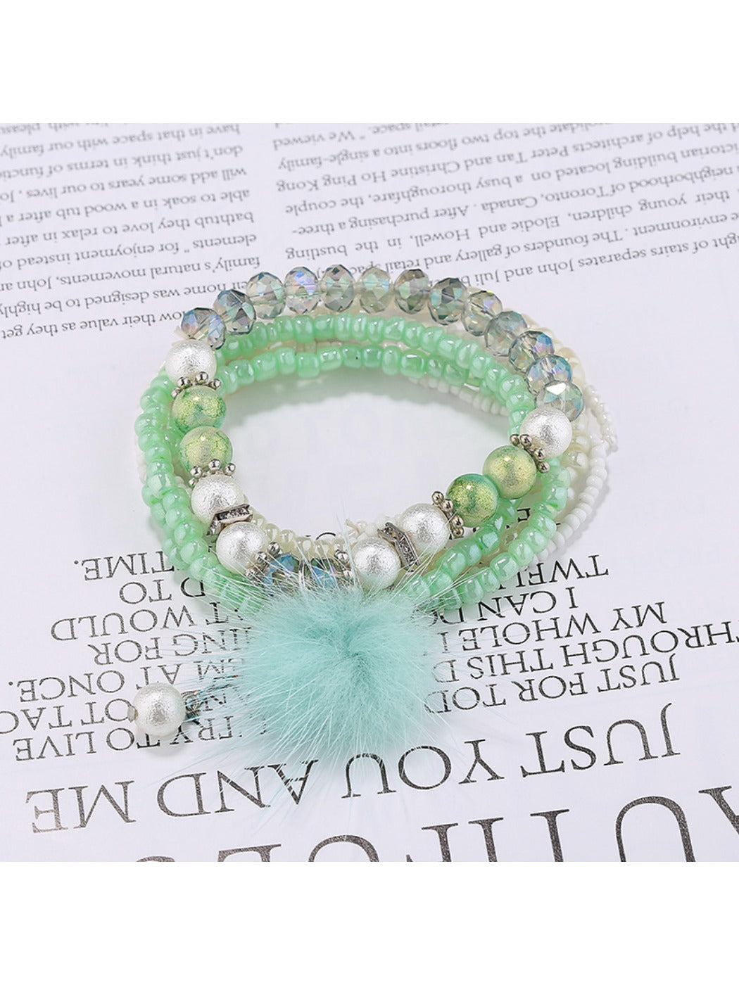 Lovra beaded bracelet with pompom pendant laid flat on white background