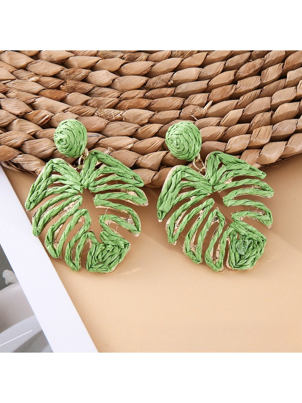 Model wearing raffia woven hollow leaf shaped earrings with a neutral outfit