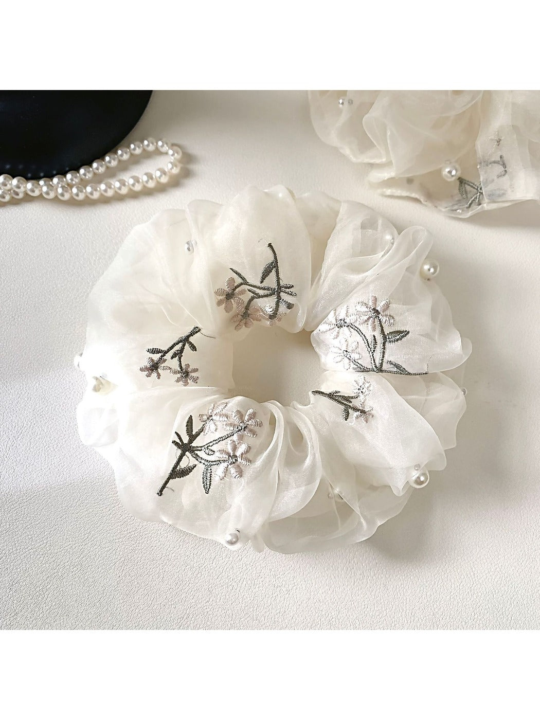 White floral scrunchie displayed on a light background showing its elastic and gathered fabric