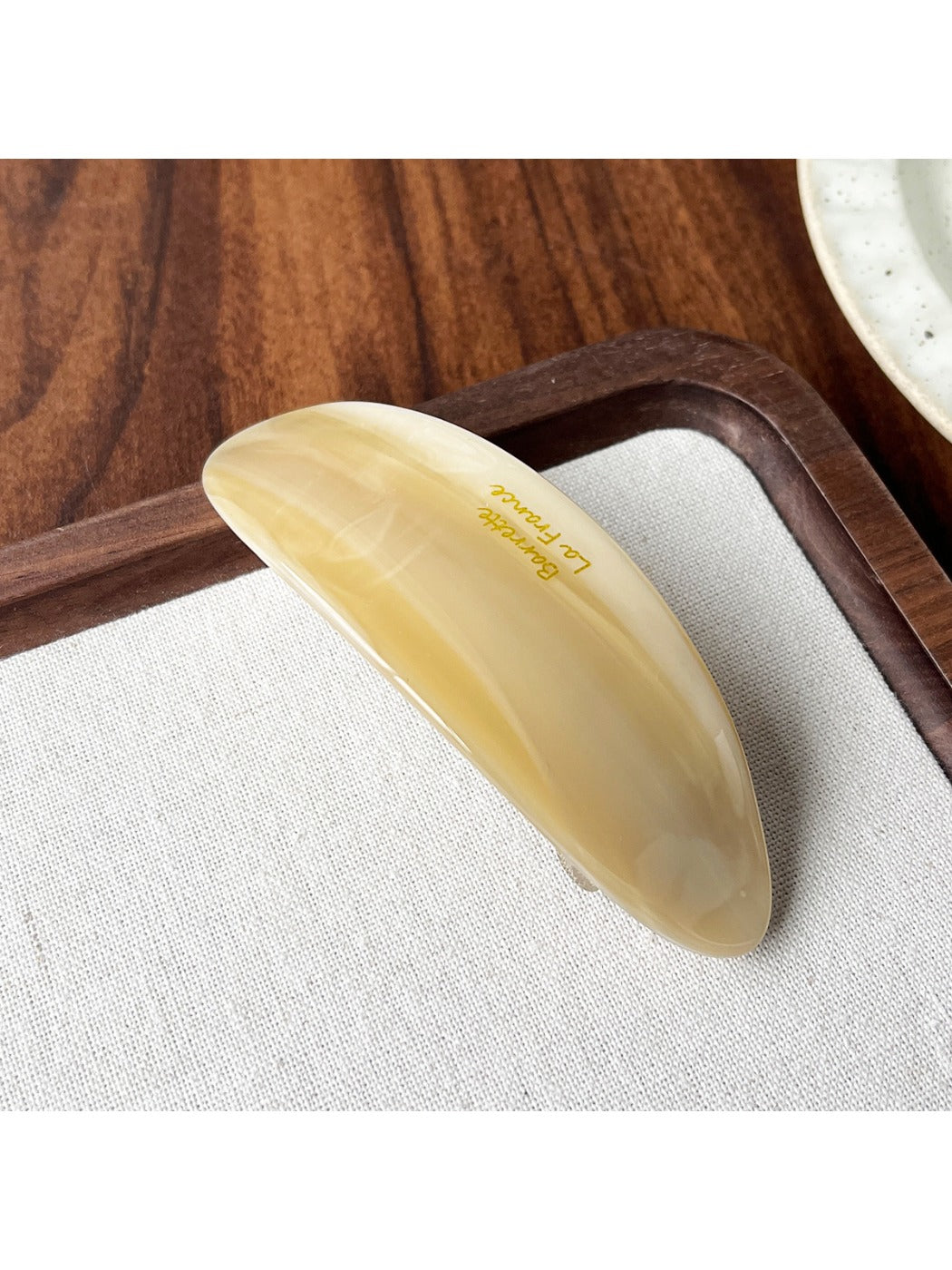 Beau oval hair clip positioned diagonally on a neutral fabric background