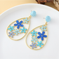 Pair of Earedge floral raffia statement drop earrings on a wooden surface