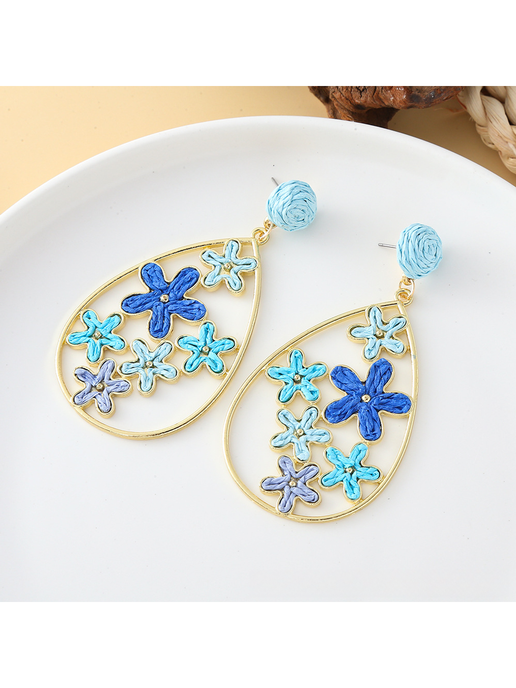 Pair of Earedge floral raffia statement drop earrings on a wooden surface