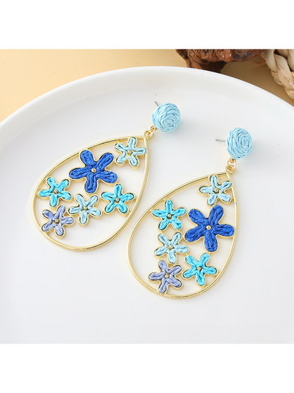 Pair of Earedge floral raffia statement drop earrings on a wooden surface
