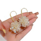 Hydrangea shaped drop earrings hanging from a jewelry stand with soft lighting