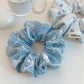 Blue scrunchie with white bows wrapped around a wrist