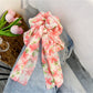 Red floral print bow scrunchie held in hand against neutral background