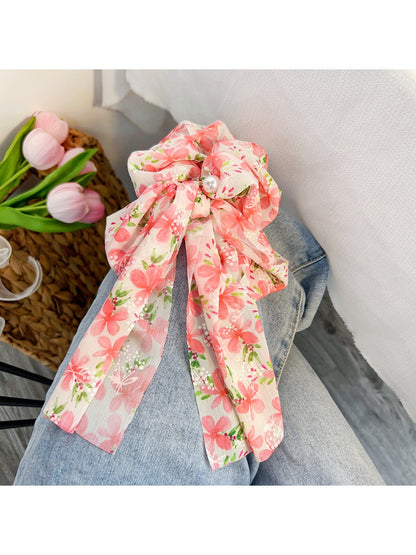Red floral print bow scrunchie held in hand against neutral background