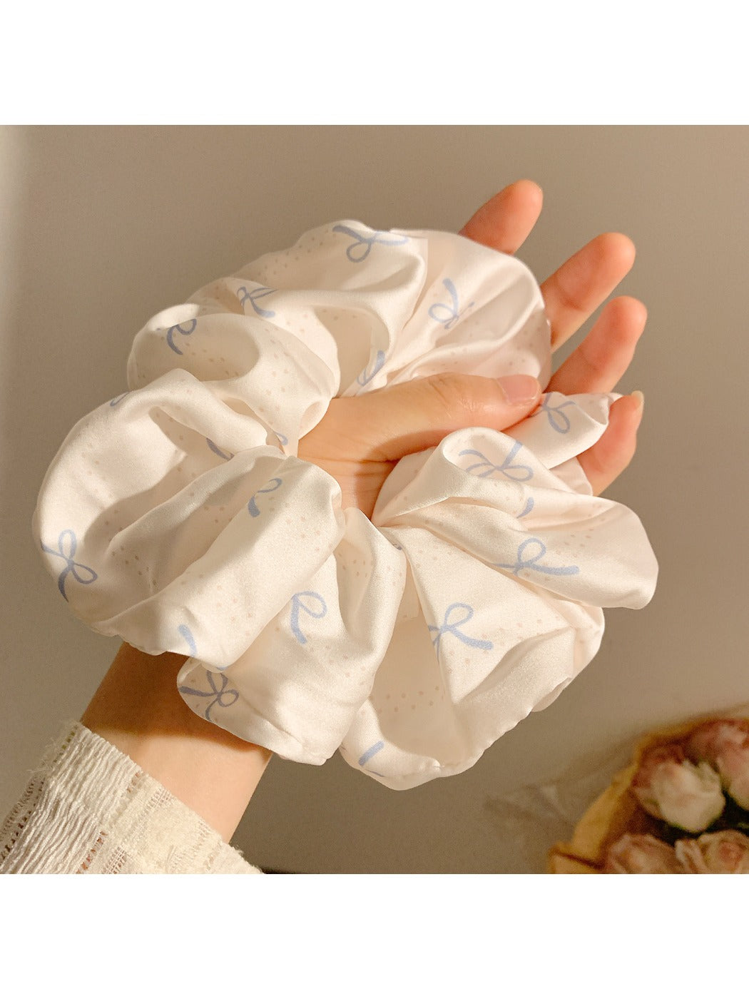 Satin scrunchie with minimalist bow pattern displayed on a hand