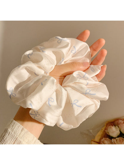 Satin scrunchie with minimalist bow pattern displayed on a hand