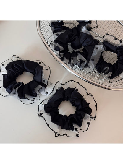 Black scrunchie with polka dot trim styled on a model's wrist