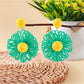 Pair of raffia flower shaped drop earrings laid flat on a wooden surface