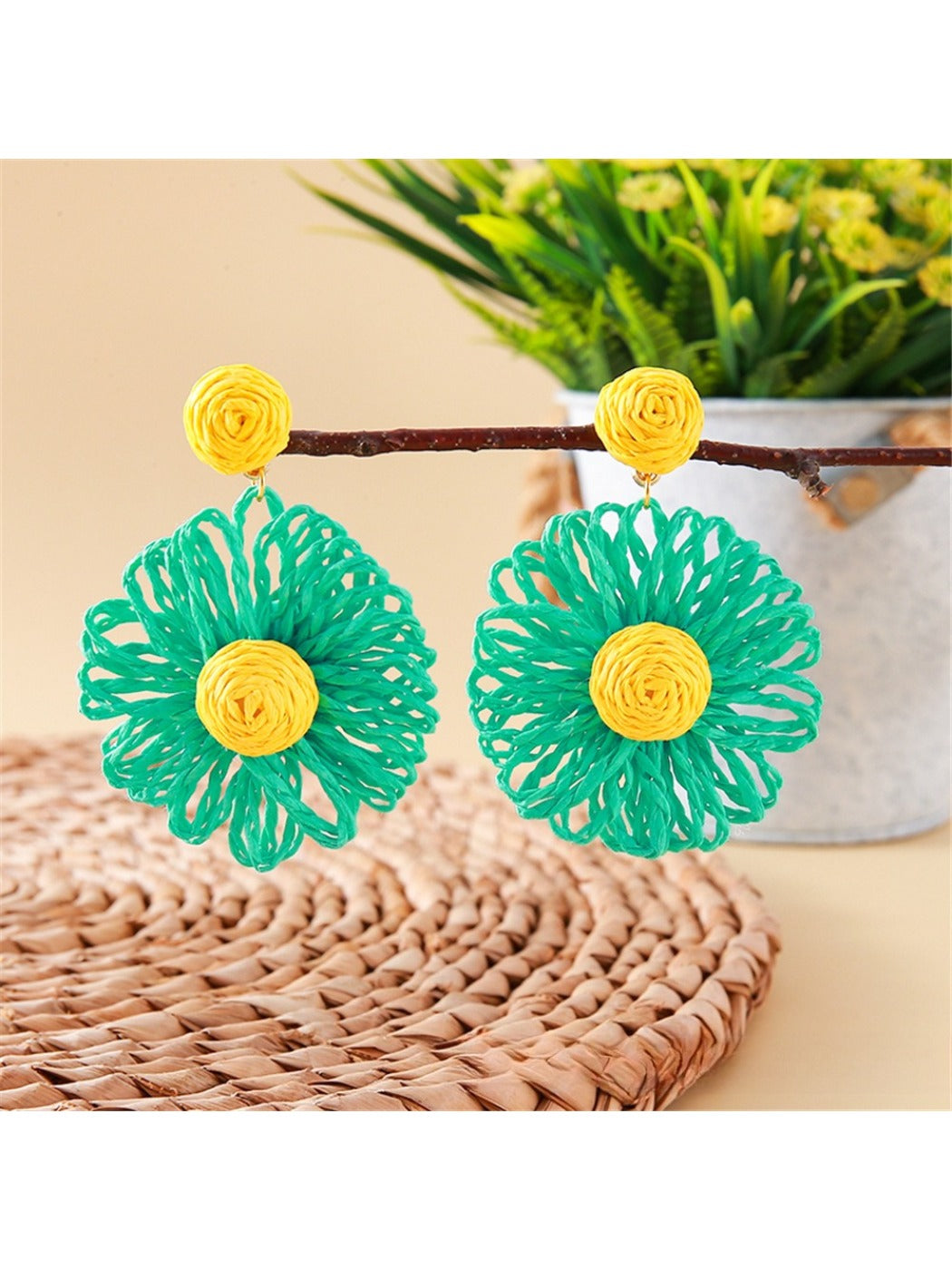 Pair of raffia flower shaped drop earrings laid flat on a wooden surface