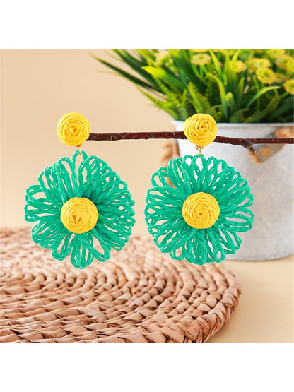 Pair of raffia flower shaped drop earrings laid flat on a wooden surface