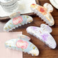 Beau hair clip showing multicolored floral design on a curved clip base