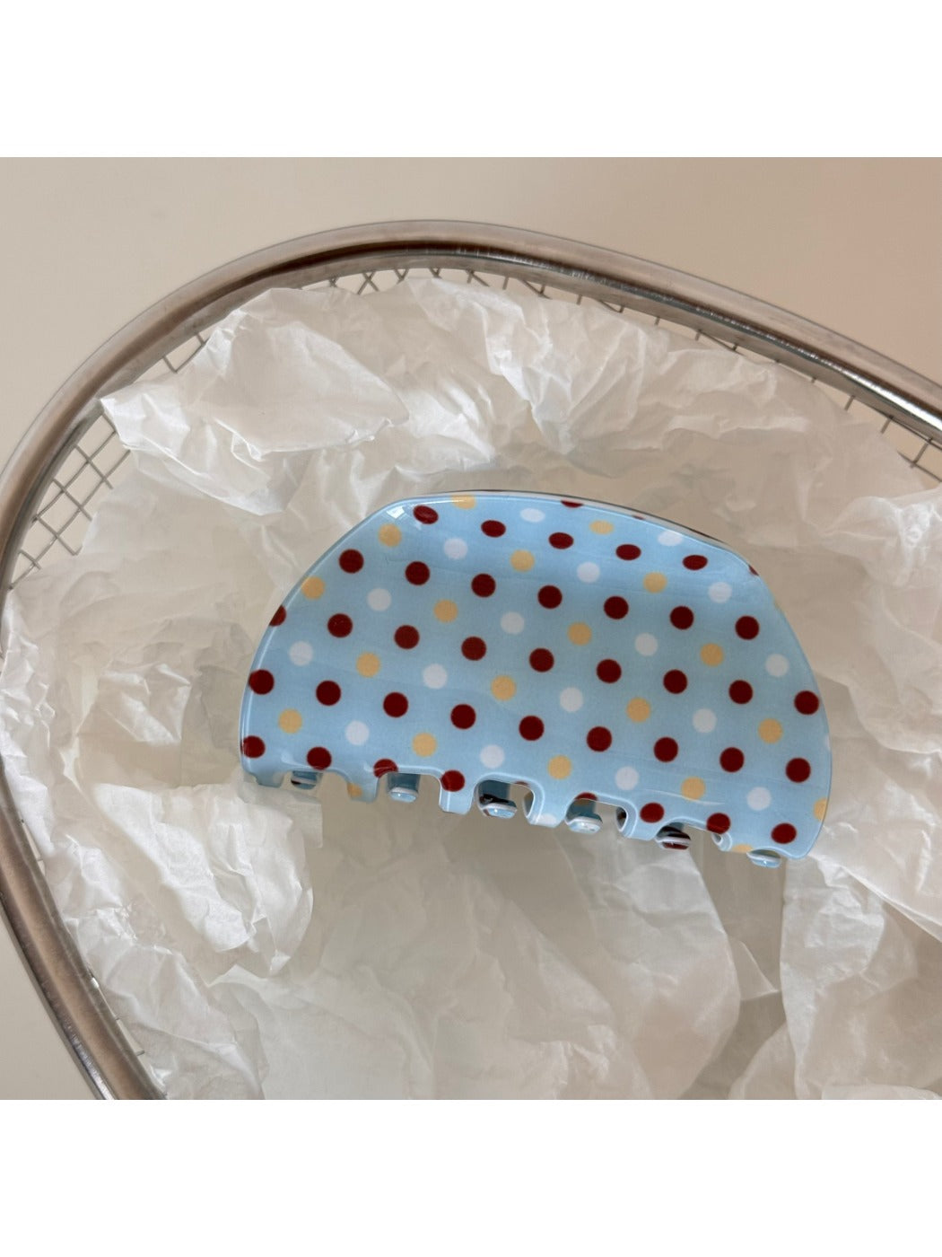 Blue polka dot hair clip held in hand against neutral background