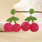 Raffia woven cherry earrings shown from above on a neutral background