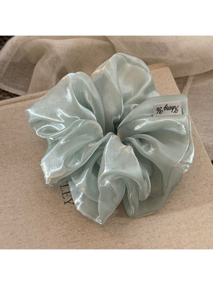 Model wearing a beige satin ruched scrunchie holding hair in a ponytail