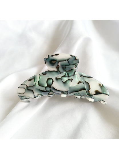 Beau vintage acetate claw clip resting on wooden surface with soft shadows