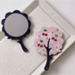 Mirroray tree-shaped handheld mirror reflecting a bright room interior