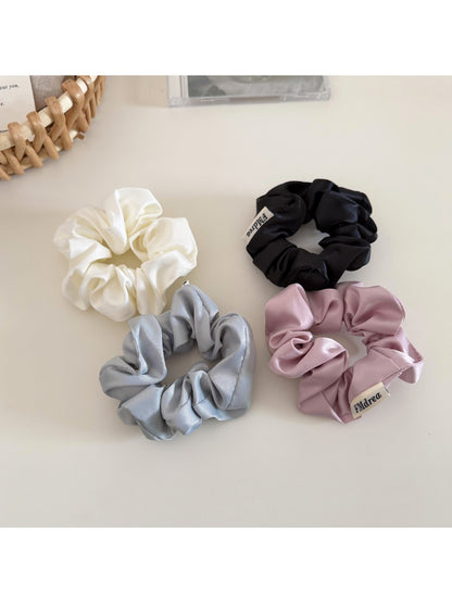 Top view of a beige satin bow scrunchie showing its smooth texture and bow detail