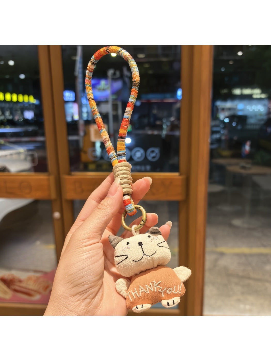 Silver cat charm keychain attached to a set of keys on a wooden surface