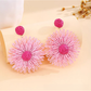 Pair of vibrant floral raffia drop earrings displayed on a wooden surface