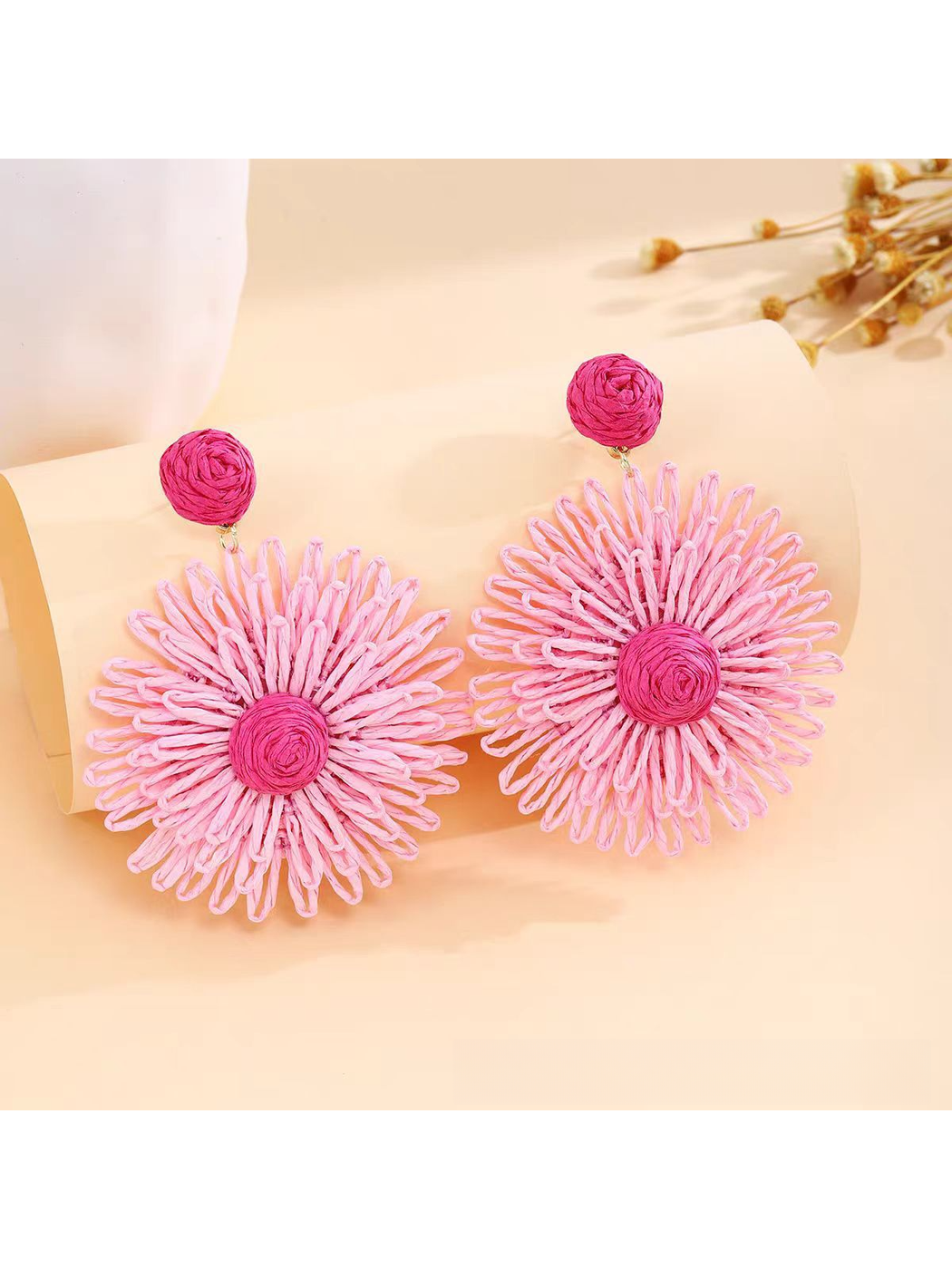 Pair of vibrant floral raffia drop earrings displayed on a wooden surface