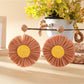 Raffia sunflower earrings placed on a wooden surface with natural lighting