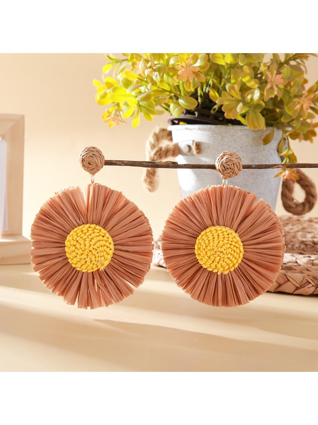 Raffia sunflower earrings placed on a wooden surface with natural lighting