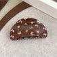 Beau claw clip resting on wooden surface with butterfly design visible