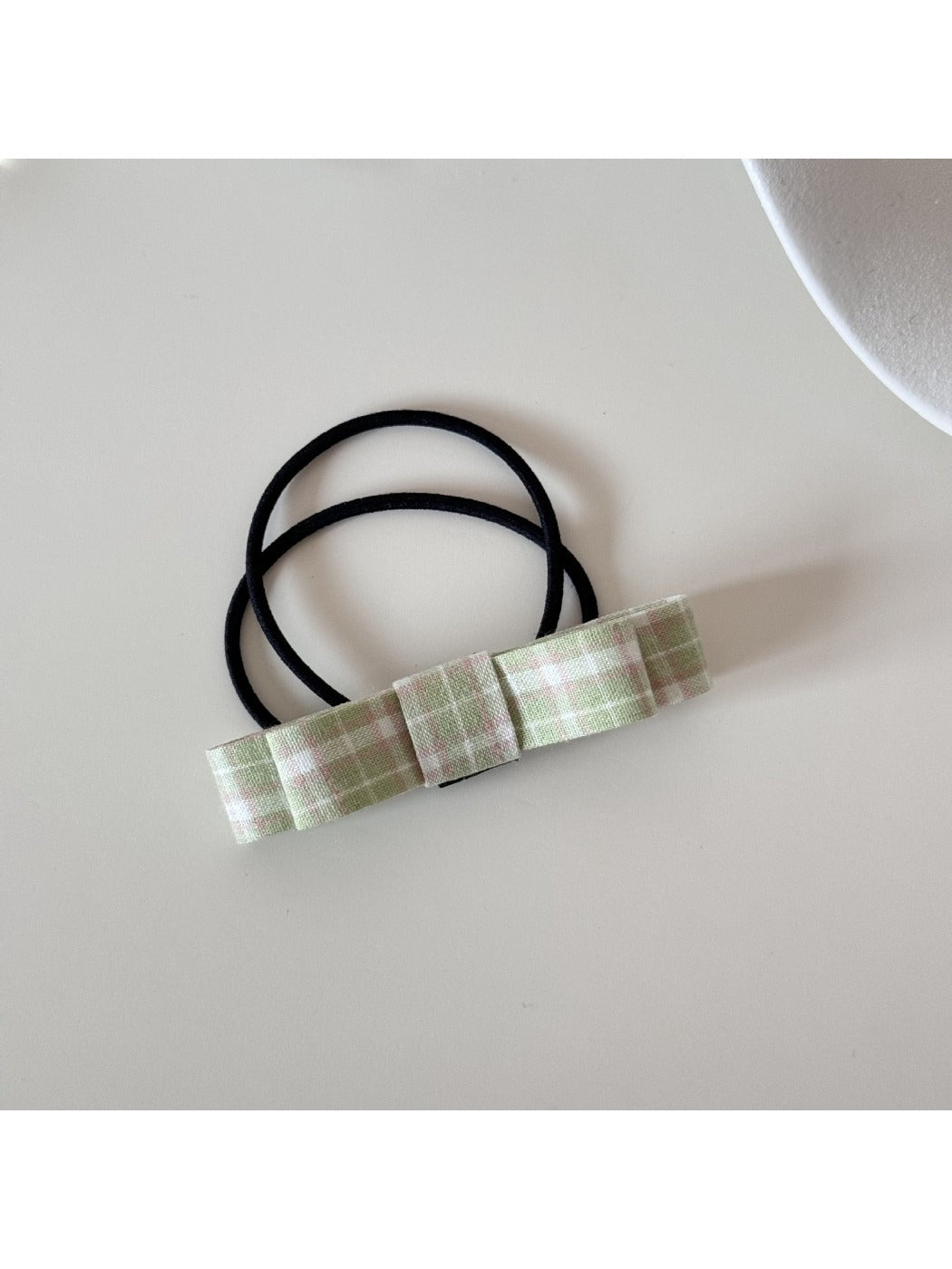 Pink bow hair tie displayed on a white ceramic dish for styling inspiration