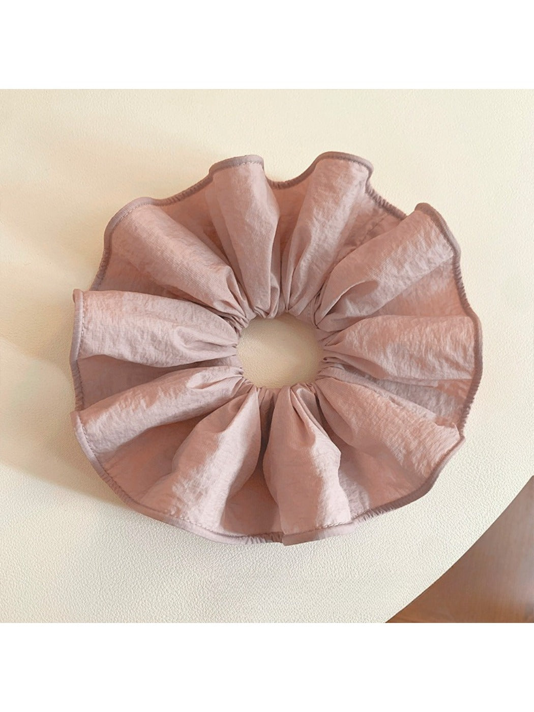 Soft pink scrunchie packaged in a clear plastic bag with branding