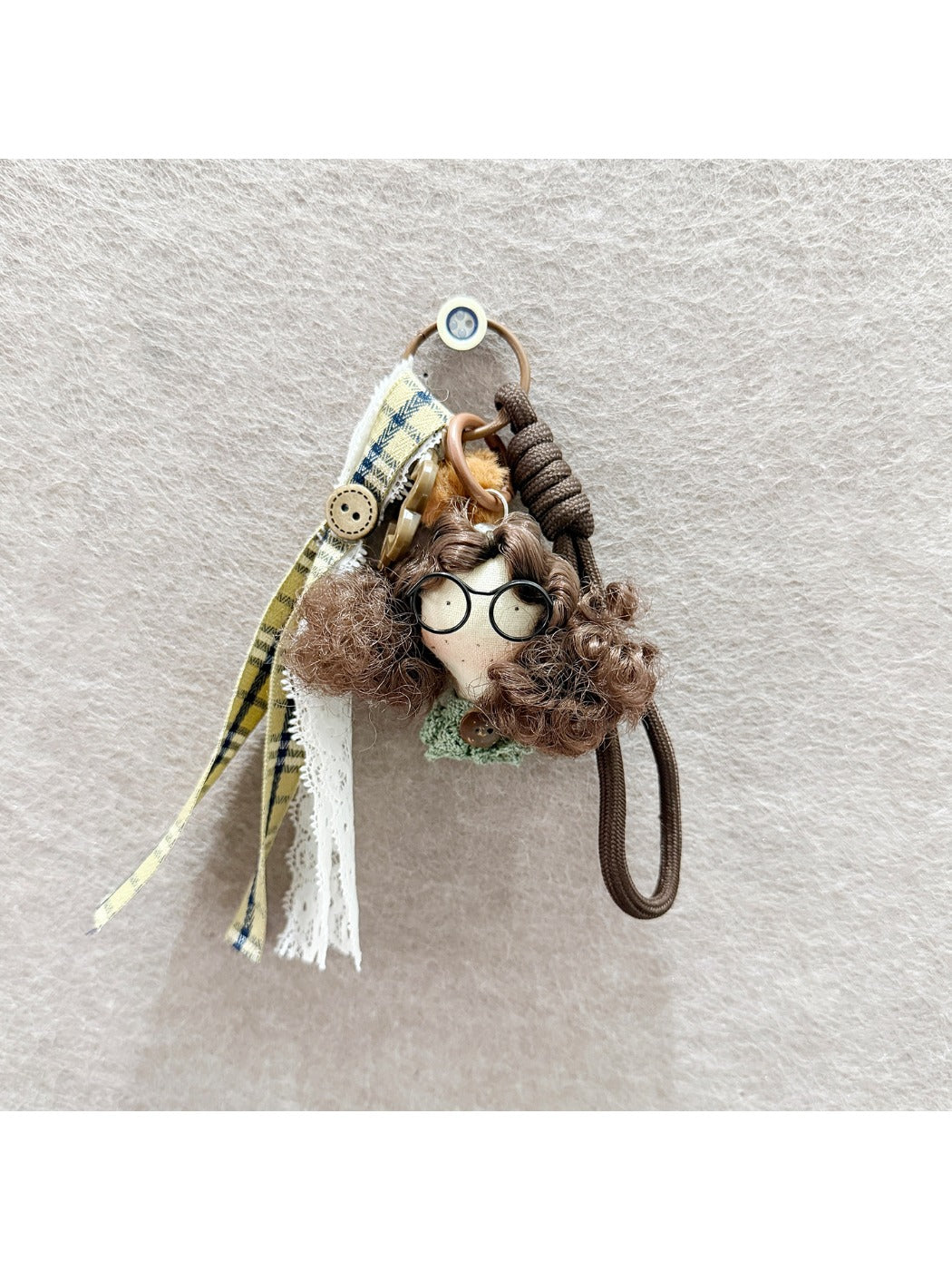 Fabric doll keychain displayed on a wooden surface with vibrant curly hair