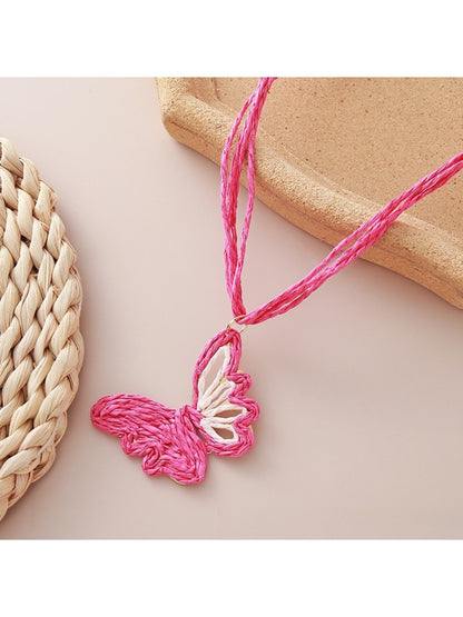 Earedge raffia butterfly pendant necklace displayed on a wooden surface