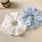 Side view of a modern ruched scrunchie in a solid color on a flat surface