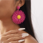 Colorful floral raffia earrings hanging on a decorative stand