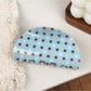 Blue polka dot hair claw clip displayed on a fabric background