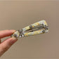 Yellow hair clip with small white and orange flowers held in hand against a neutral background