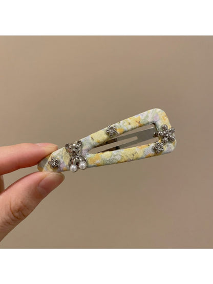 Yellow hair clip with small white and orange flowers held in hand against a neutral background