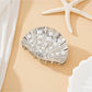 Beau seashell hair clip worn in blonde hair against a beach background