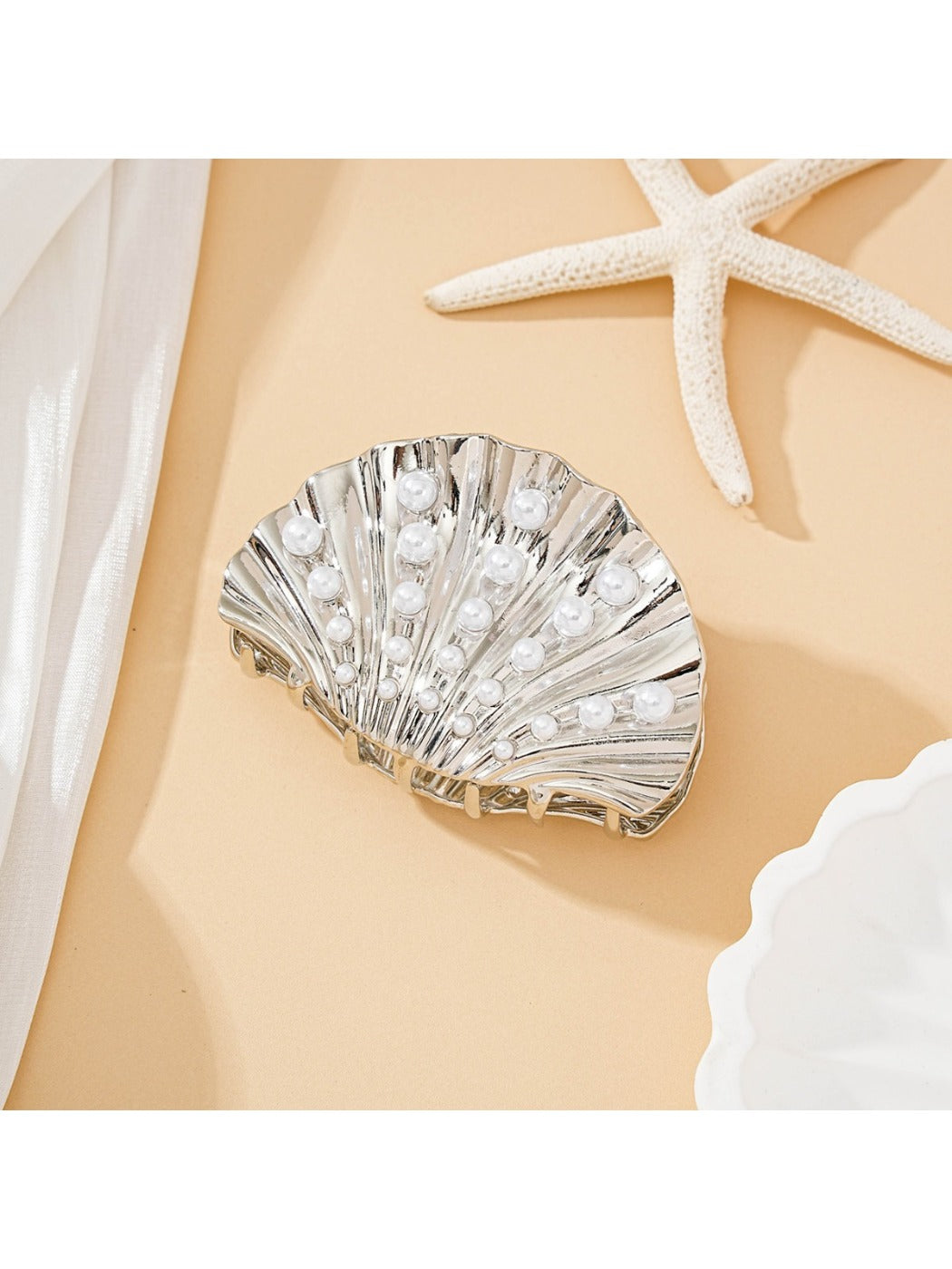 Beau seashell hair clip worn in blonde hair against a beach background