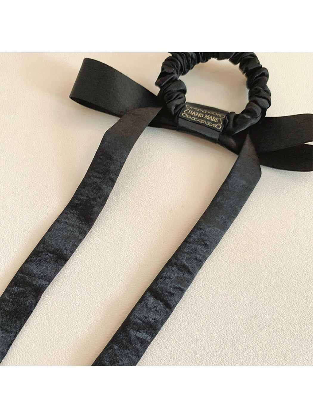 Satin bow hair tie displayed on a wooden surface with natural lighting