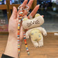 Keypus kitty charm with a small bell attached, displayed on a wooden table