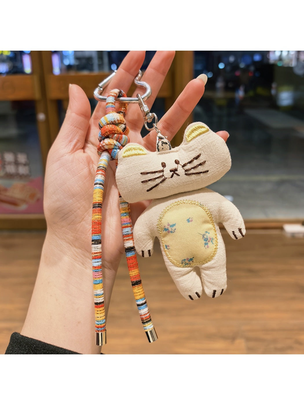 Keypus kitty charm with a small bell attached, displayed on a wooden table