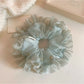 Close-up of Gifty tulle ruffle scrunchie with white polka dots on black fabric