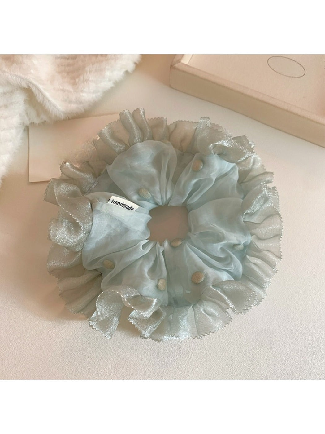 Close-up of Gifty tulle ruffle scrunchie with white polka dots on black fabric
