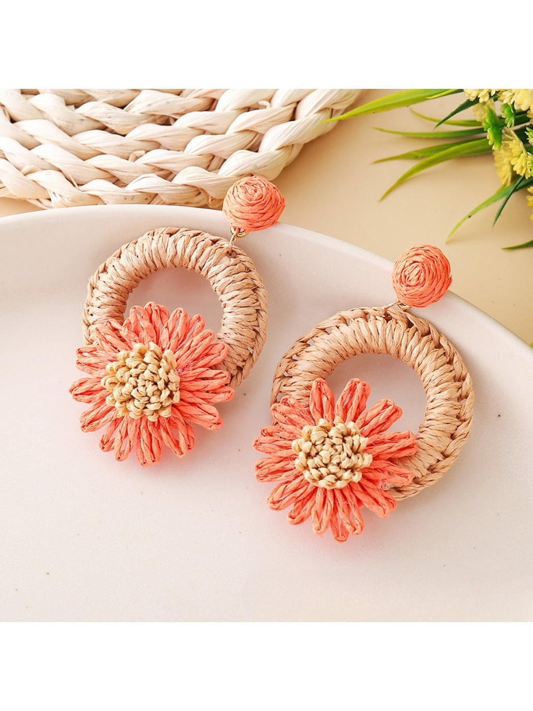 Earedge raffia daisy stud earrings placed next to green leaves for styling